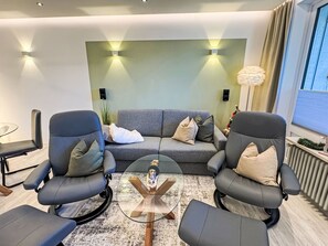A modern living room with a grey sofa, two armchairs, a glass coffee table, and a decorative plant. - Ferienwohnung für 2-3 Personen by Interhome (Goslar)