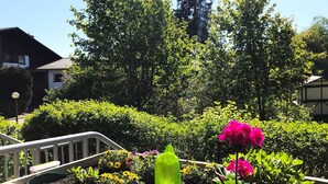 Un jardin avec différentes plantes et fleurs, une rambarde en métal et un bâtiment en arrière-plan.