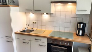 Une cuisine moderne avec des meubles blancs, un four en acier inoxydable, une machine à café et un plan de travail en bois.