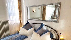 Un lit bien fait, avec une literie à rayures et plusieurs oreillers, une lampe de chevet et un miroir au mur.