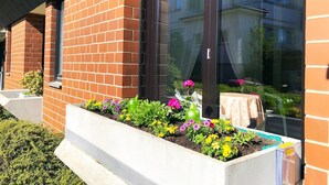 Un bâtiment à la façade en briques, doté de grandes fenêtres et agrémenté d’un parterre fleuri où poussent différentes plantes et fleurs.