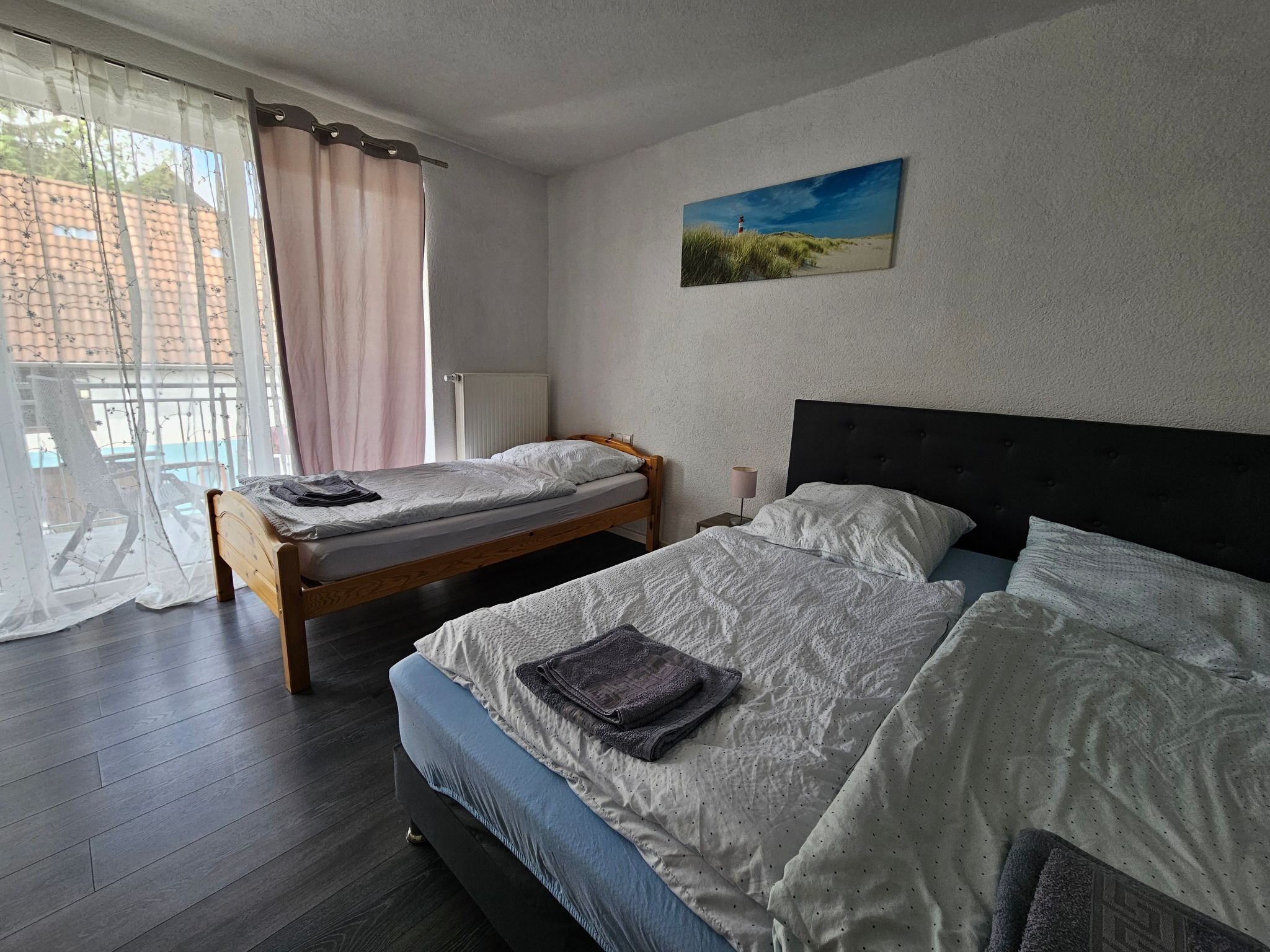 Ein Schlafzimmer mit zwei Betten, einem Fenster mit Vorhängen, einem Heizkörper und einem Gemälde an der Wand.
