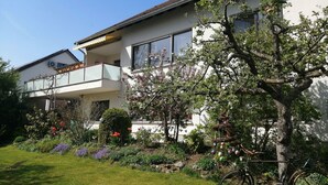 A two-story house with a balcony, surrounded by a garden with various plants and flowers. - Große Ferienwohnung in Sinbronn mit Garten by Interhome (Dinkelsbühl)