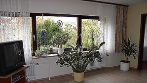 A living room with a television on a stand, a potted plant, and a window with curtains. - Große Ferienwohnung in Sinbronn mit Garten by Interhome (Dinkelsbühl)