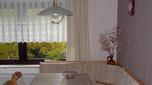 A dining area with a table and bench seating, a hanging light fixture, a window with curtains, and a radiator. - Große Ferienwohnung in Sinbronn mit Garten by Interhome (Dinkelsbühl)