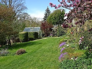 Ein gepflegter Garten mit vielfältigen Pflanzen und Blumen, einem gut ausgebauten Weg und einem Wintergarten mit Glasdach.