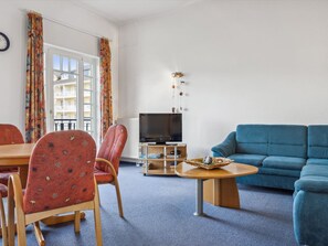 Ein Wohnzimmer mit einem blauen Sofa, roten gemusterten Stühlen, einem Holztisch und einem Fernseher.