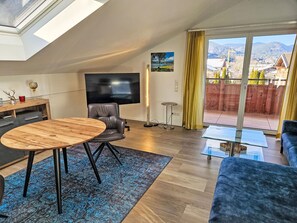 A modern living room with a wooden dining table, a leather sofa, a TV, and a balcony with a view of mountains. - Tegernsee Stern bei Rottach-Egern by Interhome (Rottach-Egern)