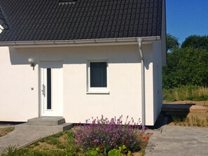 Una casa de una sola planta con fachada blanca, techo de tejas oscuras y una ventana pequeña.