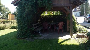 Un gazebo in legno con tavolo e sedie, immerso nel verde.