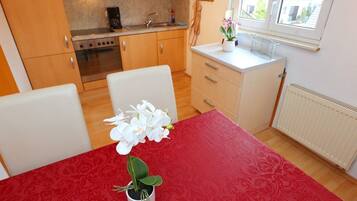 A compact kitchen with wooden cabinets, a stove, and a sink. There's a dining table with a red tablecloth and a potted orchid.