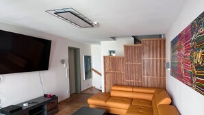 Ein modernes Wohnzimmer mit einem großen Flachbildfernseher, einem Ecksofa und einer Wand aus Holzlamellen.