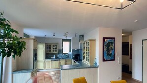Eine moderne Küche mit hellen Holzschränken, einer zentralen Kochinsel und einem Essbereich mit gelben Stühlen.