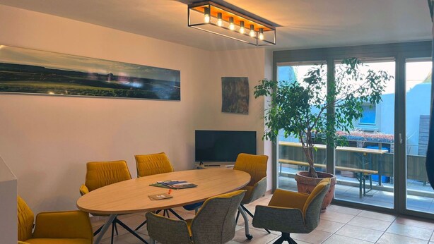 Ein moderner Konferenzraum mit einem großen ovalen Tisch, gelben Stühlen, einem Flachbildfernseher und einem großen Fenster mit Blick ins Freie.