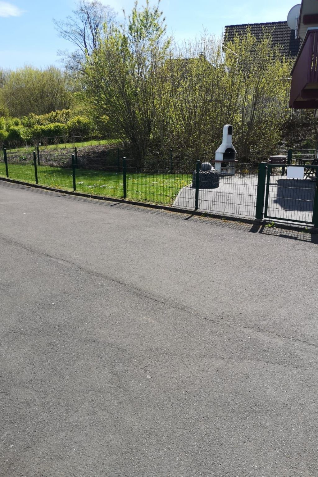 A paved road with a metal fence and greenery in the background.