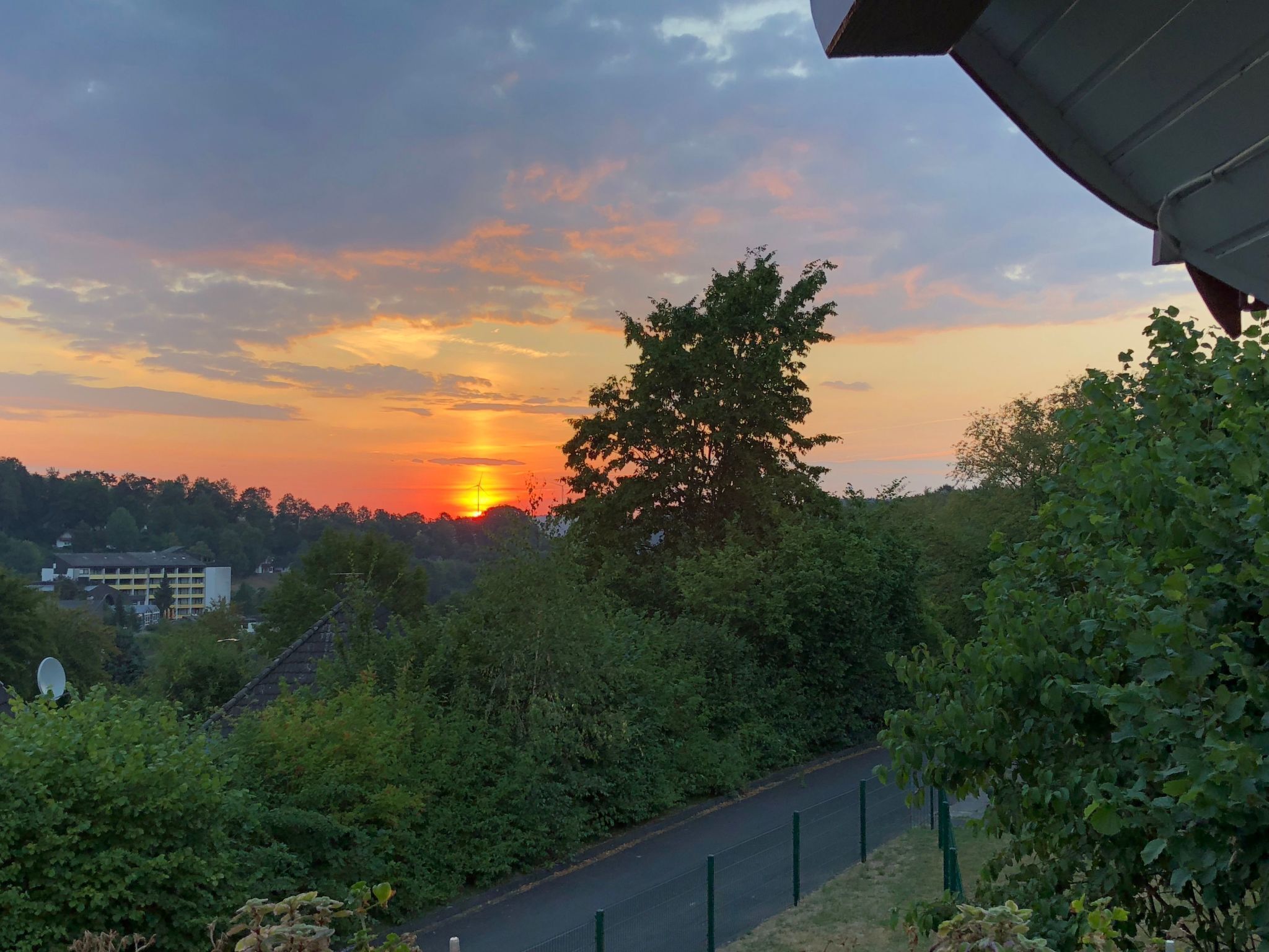 A sunset with a tree in the foreground and a building in the background.