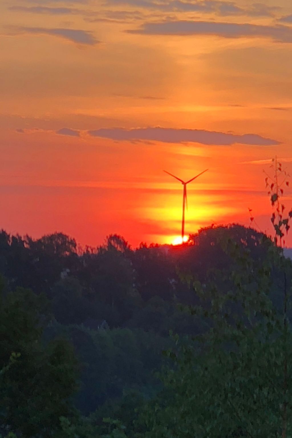 Ein Sonnenuntergang mit einer gegen den Himmel abgesetzten Windkraftanlage.