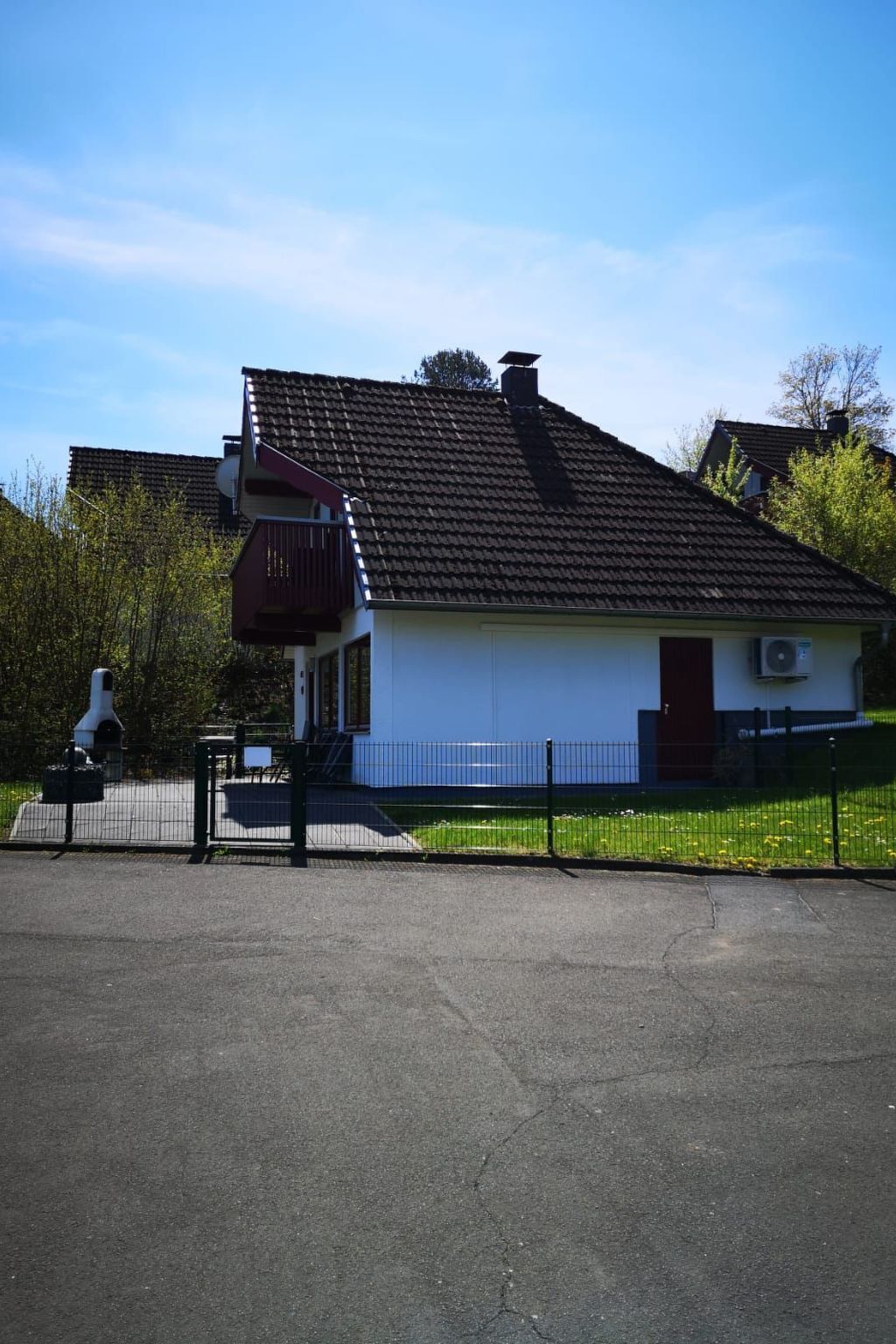 Ein eingeschossiges Haus mit einem dunklen Ziegeldach, einer kleinen Veranda und einem eingezäunten Garten.