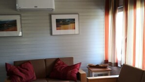 A cozy room with a sofa, a small table, and a chair. There is a window with curtains and a picture frame on the wall. - Stausee in Kirchheim Seepark by Interhome (Kirchheim)