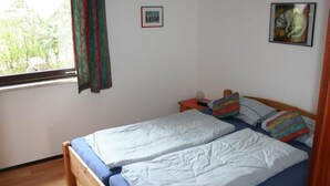 A bedroom with a wooden bed, a nightstand, a window with curtains, and two framed pictures on the wall. - Hetzberghaus by Interhome (Laubach)