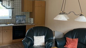 Un espacio habitable compacto con kitchenette, dos sillones de cuero negro, una mesa de madera y una lámpara colgante.