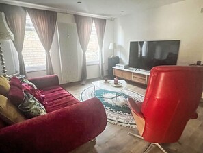 Olohuoneessa on punainen sohva, punainen nojatuoli, televisio ja pieni pöytä, jonka päällä on kynttilöitä.