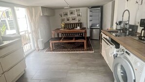 Een compacte keuken met een wasmachine, een eethoek met een bank en een koelkast.