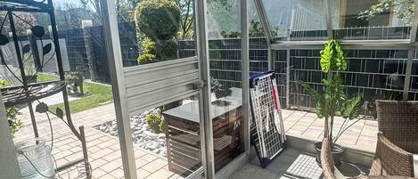 Une véranda dotée d’une porte en verre, d’une table en métal et de meubles en osier.