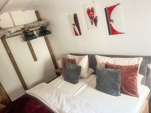 A bedroom with a bed, pillows, a hanging shelf, and wall art.