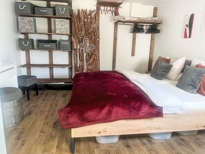 Makuuhuoneessa on puinen sänky, punainen heittopeitto, puinen pääty, hylly säilytyslaatikoineen ja seinälle kiinnitetty naulakko.