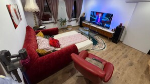 Een moderne woonkamer met een rode bank, een glazen salontafel en een televisie waarop een nieuwsuitzending draait.