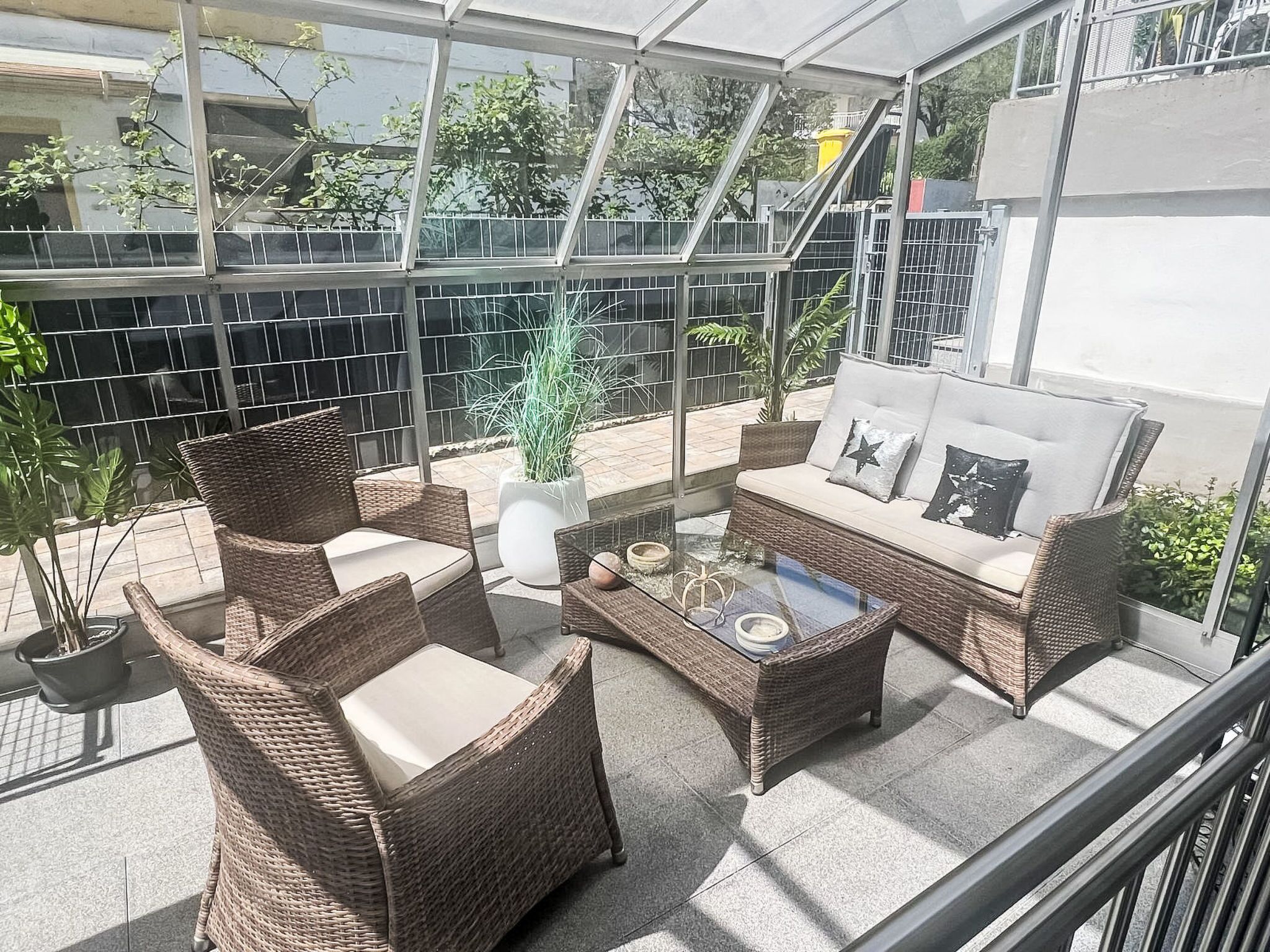 Eine sonnendurchflutete Terrassenanlage mit Korbmöbeln, einem Glastisch und einem Blumentopf.