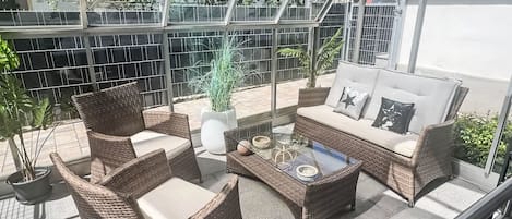 Eine sonnendurchflutete Terrassenanlage mit Korbmöbeln, einem Glastisch und einem Blumentopf.