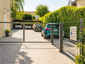 Ein durch einen Zaun gesicherter Parkbereich mit mehreren Autos, einem Schild für Gästeparkplätze und einem Gebäude im Hintergrund.