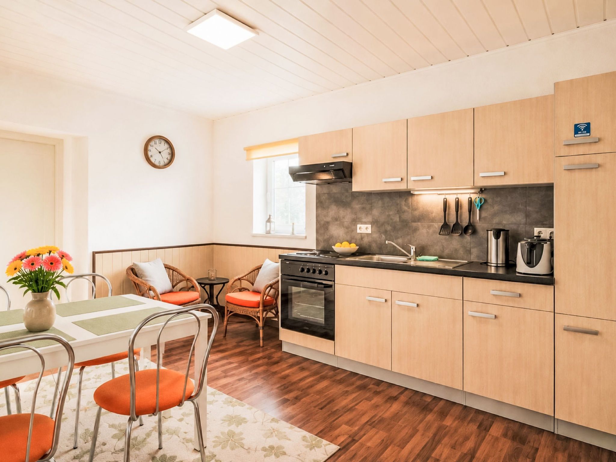 Una cucina moderna con mobili in legno, un piano cottura nero e un'area pranzo con sedie in vimini e un tavolo.