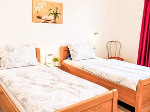 Ein Zimmer mit zwei Einzelbetten, einem Nachttisch mit Lampe, einem Wandbild und einem roten Vorhang.