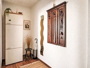 Eine Küche mit einem Kühlschrank, einem Holzkabinett mit Haken, einem gerahmten Bild und einer Vase mit Trockenblumen.