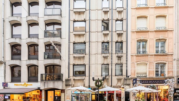 Um edifício de vários andares com uma padaria no andar térreo, uma floricultura no segundo andar e uma loja fechada no terceiro.