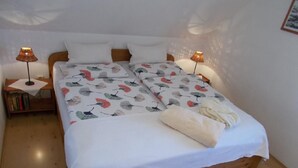 A double bed with a floral bedspread, two bedside lamps, a wooden nightstand with books, and a white rug on a wooden floor. - Apartment Mund by Interhome (Dresden)