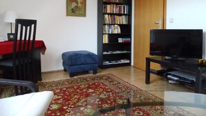 A living room with a red carpet, a bookshelf, a television, and a wooden door. - Apartment Mund by Interhome (Dresden)
