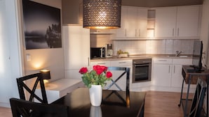 Une cuisine moderne avec des meubles blancs, un four à micro-ondes et un four traditionnel. On y trouve une table à manger avec des chaises et un vase rempli de fleurs rouges.