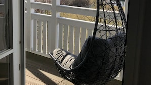 Une véranda avec un fauteuil suspendu, une balustrade blanche et une vue sur un paysage rural.