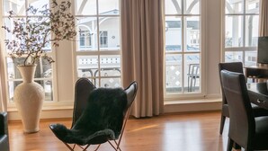 Et værelse med store vinduer, en sort læderstol, en hvid vase med en plante og et træbord.