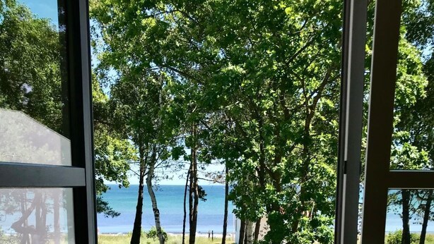 Un balcón con vista al mar, una terraza de madera y dos sillas.