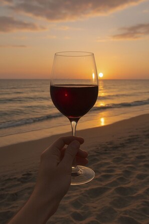 Une main tenant un verre de vin, avec un coucher de soleil en arrière-plan.
