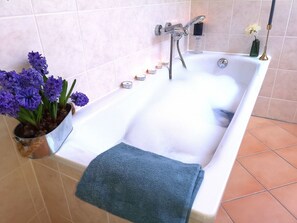 Une baignoire remplie de mousse, une serviette bleue et une plante en pot avec des fleurs violettes.