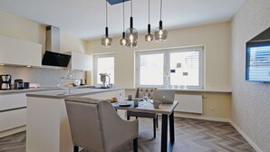 A modern kitchen with a central island, a dining area with a table and chairs, and a large window providing natural light. - Quartier 23 by Interhome (Nordhorn)