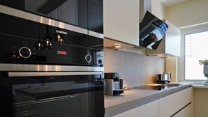 A modern kitchen with a built-in oven, a coffee machine, and a flat-screen TV mounted above the counter. - Quartier 23 by Interhome (Nordhorn)