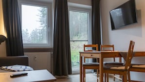 A room with a wooden table and chairs, a TV mounted on the wall, and a window with curtains. - mit zwei Schlafzimmern und Terrasse by Interhome (Weißenstadt)
