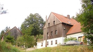 Ett rustikt trähus med ett rött tegeltak, omgivet av grönska och en stig.
